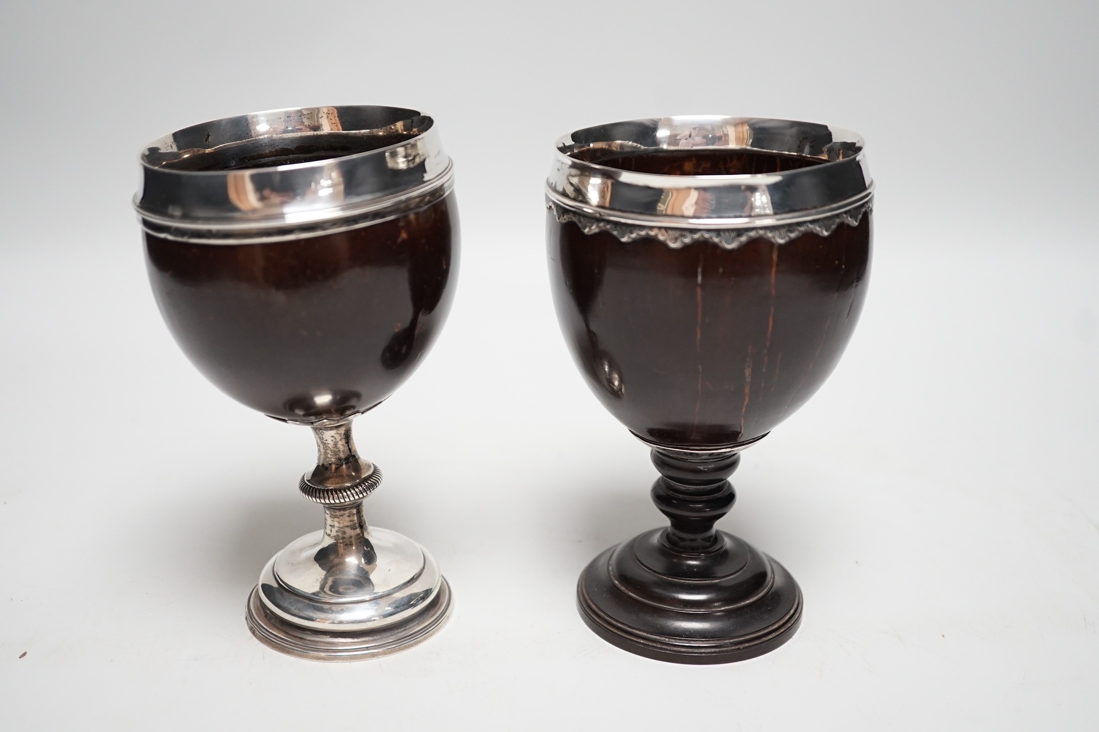 Two late 18th century white metal mounted pedestal coconut cups, one hallmarked silver for John Robbins?, London, 1764, 14.4cm, the other with white metal mounted top rim, on turned wooden base.